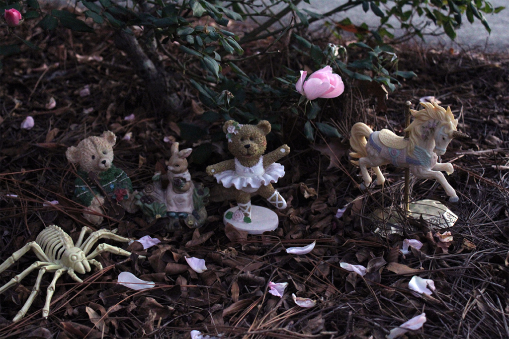 small figures sitting on dead leaves with a few fallen rose petals around